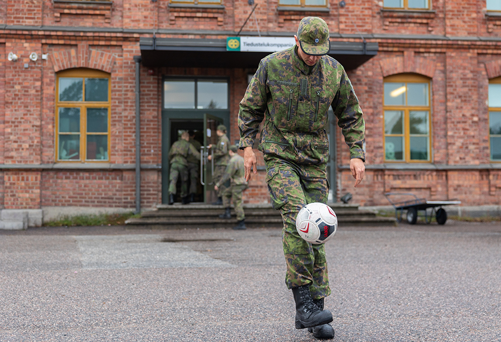 Jalkapalloilija pompottelee palloa kasarmin edessä.