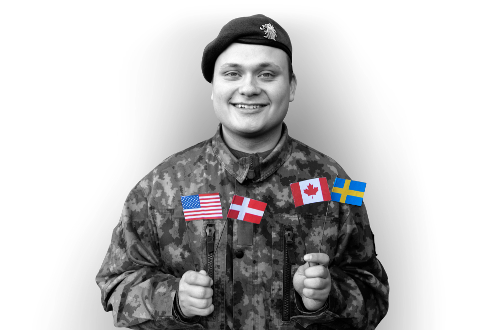 Kaartinjääkäri Nevalainen hymyilee käsissään Yhdysvaltojen, Tanskan, Kanadan ja Ruotsin liput.