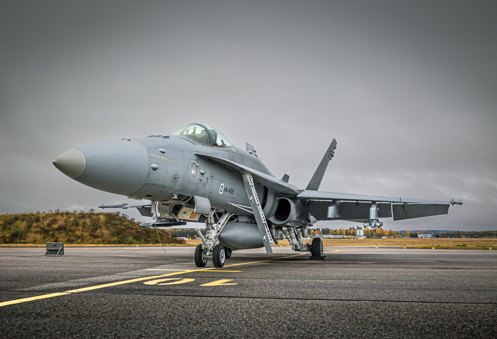 Hornetti pysäköitynä lentokentälle. Taustalla peltoa ja metsää. Harmaa taivas.