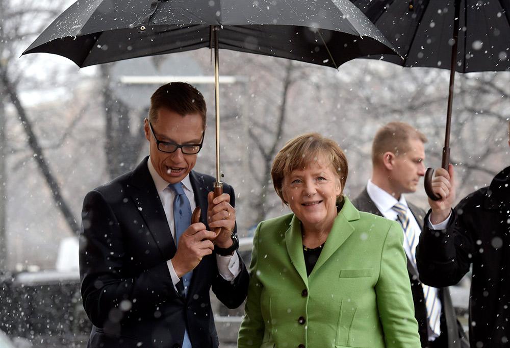1) Stubb Merkelin kanssa sateenvarjon alla. 2) Stubb triathlon-asussa.