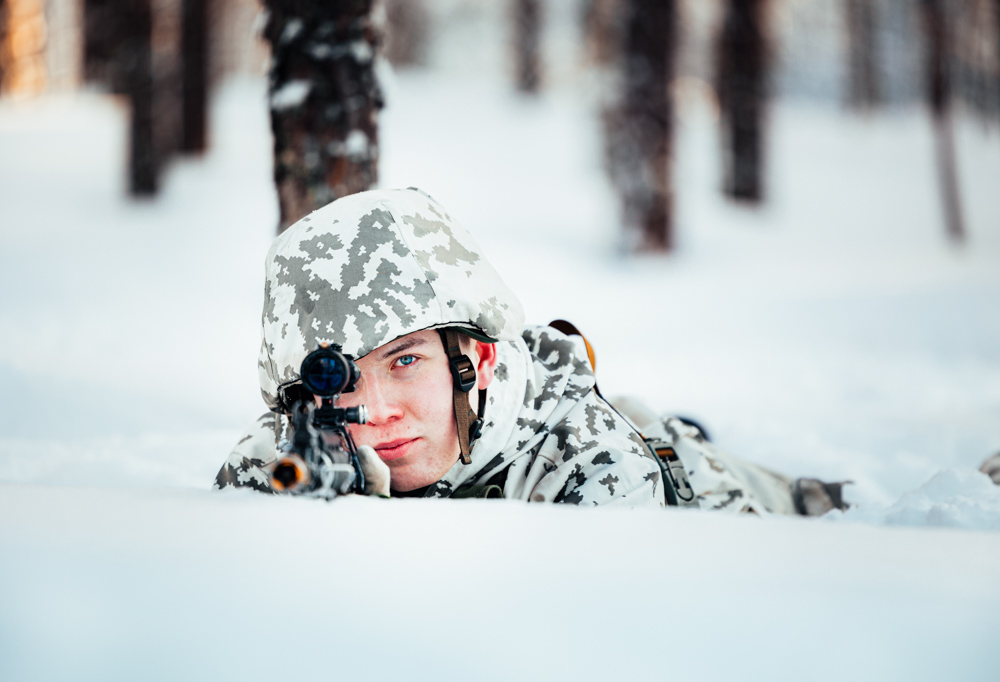 Kuvassa lumipukuinen taistelija tähtää rynnäkkökiväärillä makuultaan.