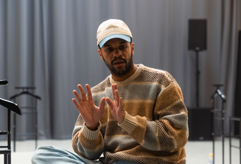 Roderick Kabanga istuu jalat ristissä, katsoo alaviistoon ja selittää käsillään.