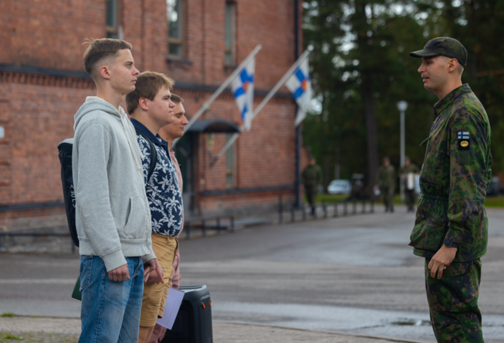 Kolme lääkintämiestä seisoo siviilivaatteet päällä luutnantin edessä.