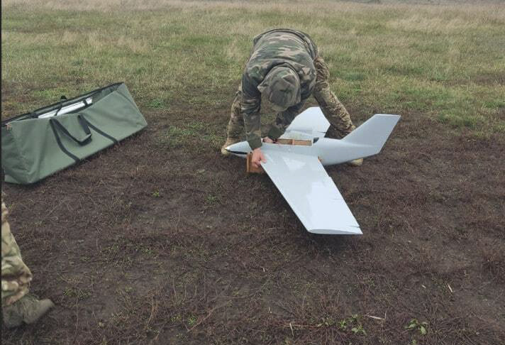 Maastopukuinen mies kumartuneena droonin ylle.