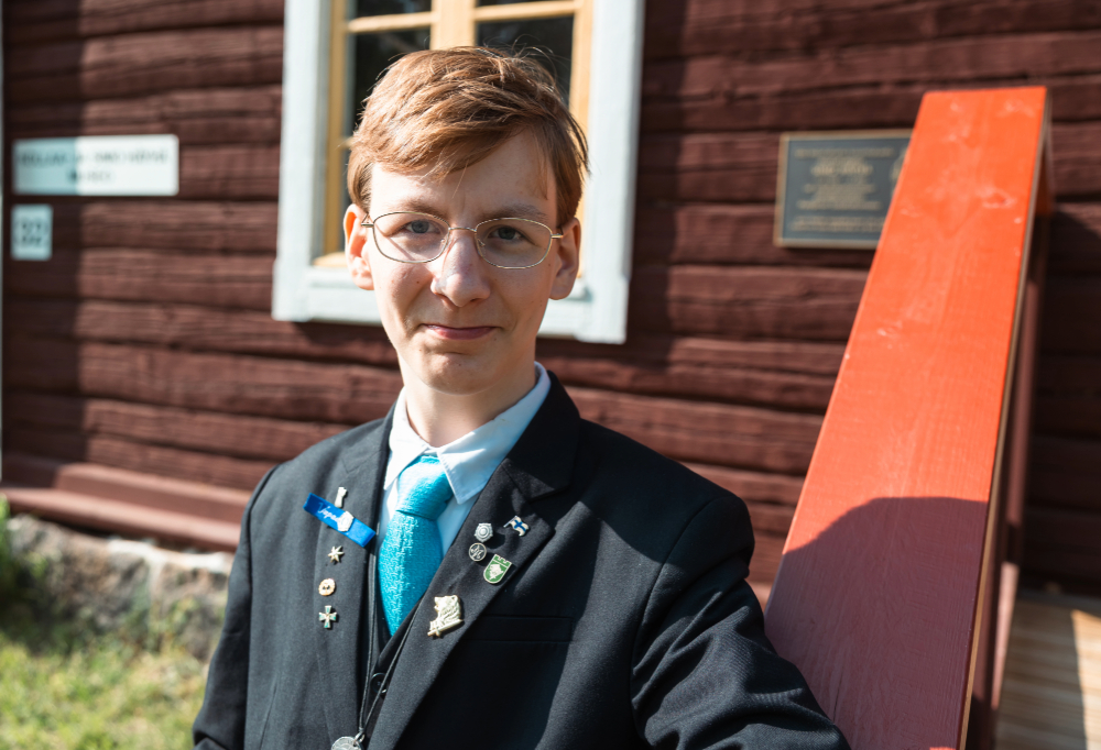 Anton Häkkänen katsoo kameraan vaisusti hymyillen punamullan värisen, vanhan rakennuksen edessä.