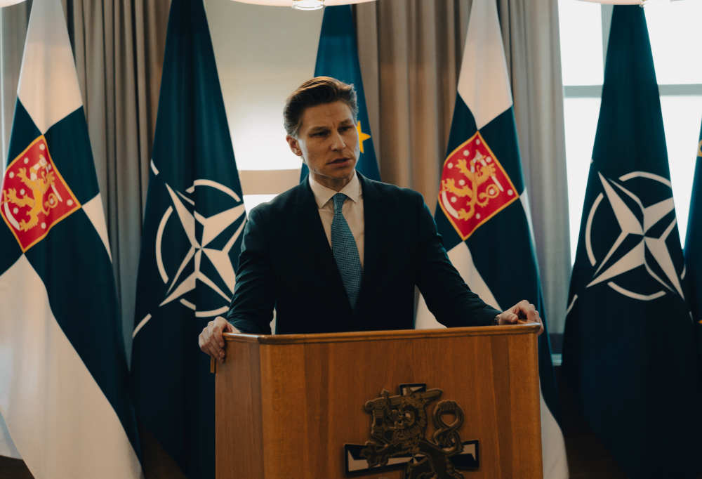 Puolustusministeri Antti Häkkänen puhujanpöntössä. Taustalla Suomen, Naton ja Euroopan Unionin lippuja.