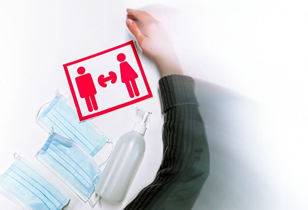 Kuvassa koronapandemiaan liittyviä esineitä, jotka symbolisesti pyyhitään pois pöydältä.