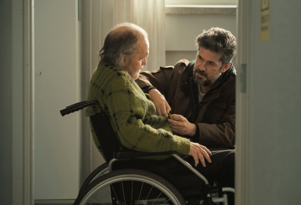 Kuvassa Tommi Korpelan esittämä hahmo Veikko on kyykyssä pyörätuolissa istuvan, Tomi Lindforsin esittämän Timon vieressä.