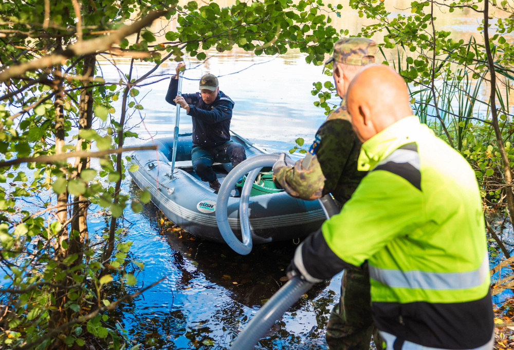 Kuvassa kolme miestä pitelee letkua, jolla imetään järvestä vettä.