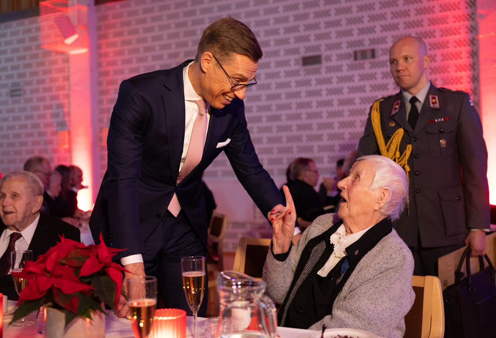 Tasavallan Presidentti Alexander Stubb tervehtimässä juhlapöydässä istuvaa lottaa.