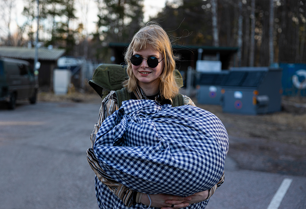 Nainen seisoo ulkona aurinkolasit päässä ja hymyilee kameralle.