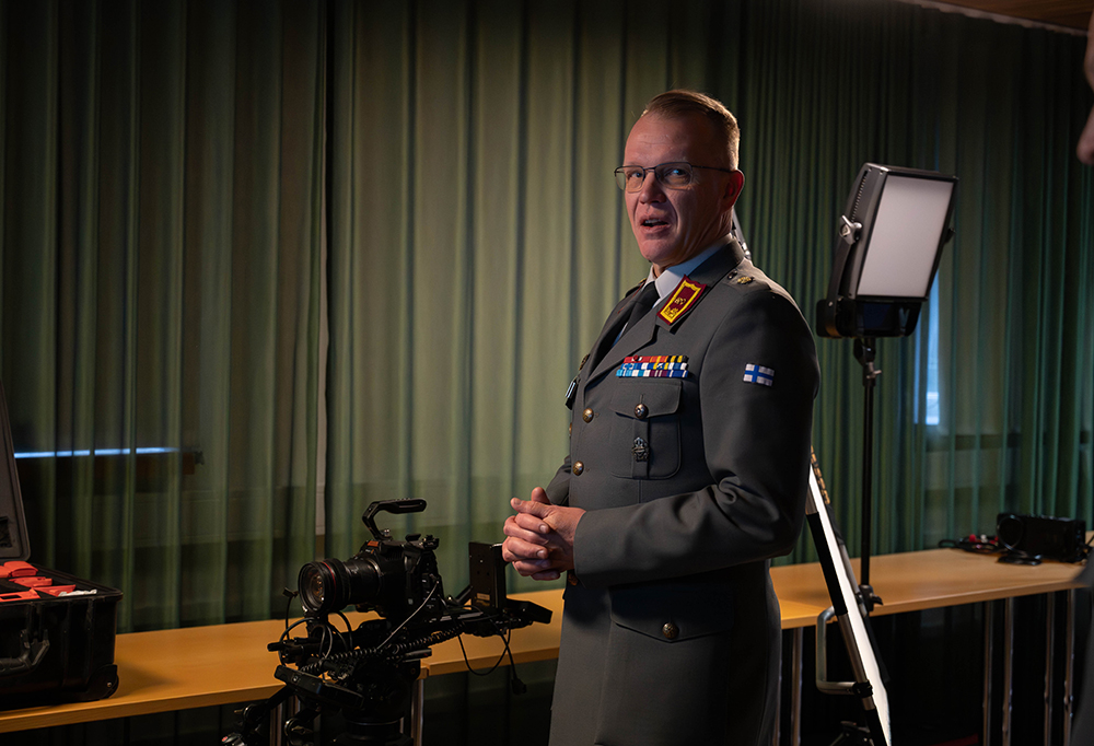 Prikaatikenraali Vesa Valtonen seisoo näyttelytilassa. Taustalla kuvauskalustoa ja valo.