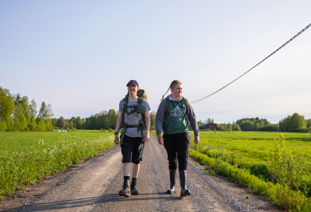 Rinkoin varustautuneet nuoret patikoivat peltoa halkovaa hiekkatietä pitkin.