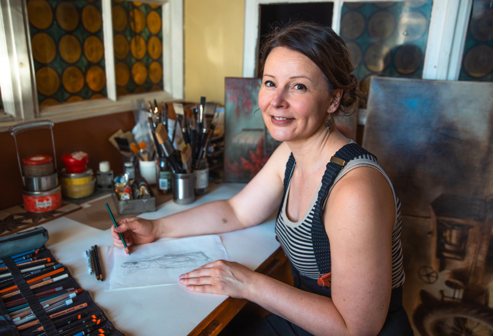 Eeva Meltio luonnostelee piirrosta paperille ja katsoo kameraan.