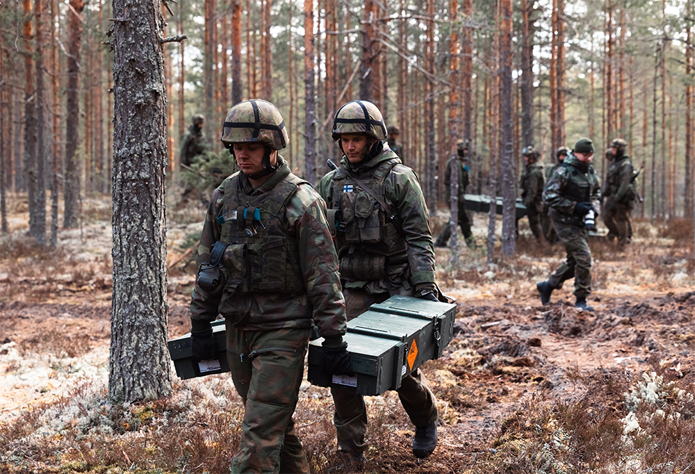 Taistelijat siirtävät pareittain raskasta lastia metsässä.