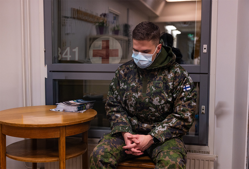 Maskilla varustautunut varusmies odottaa tuolilla istuen.