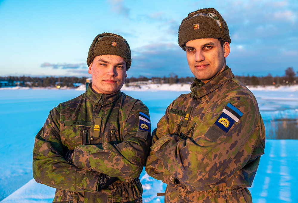 Kadetit katsovat kameraan ja pitävät käsiään puuskassa. He seisovat jäätyneen vesistön edessä.