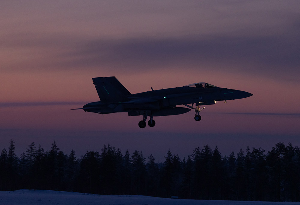 Hävittäjä lentämässä öisellä taivaalla auringonlaskun aikaan.