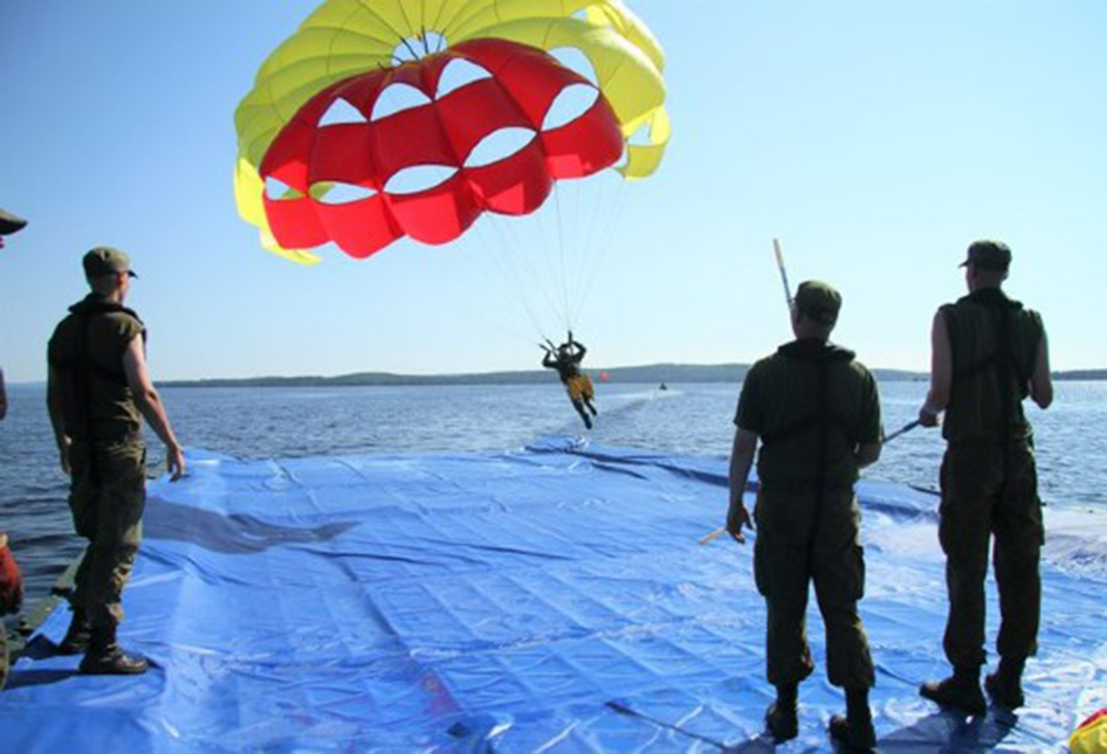 Lentäjä laskeutuu hinausvarjon avulla pelastautumislautalle.