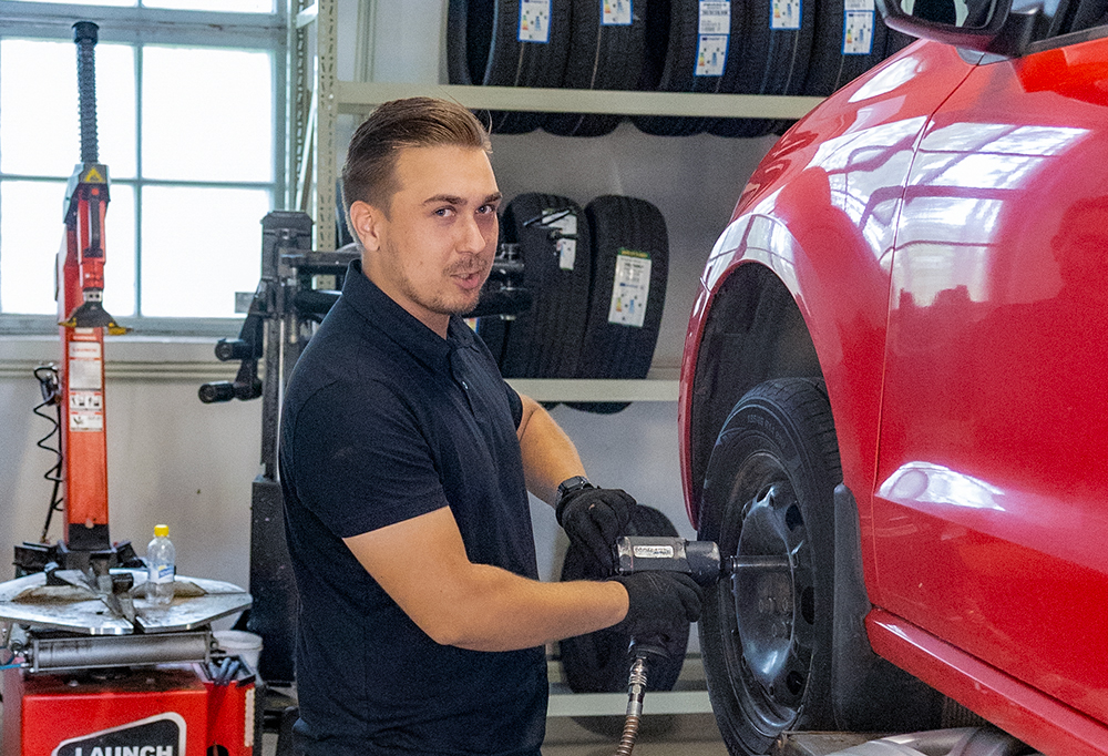 Yrittäjä vaihtamassa rengasta punaiseen henkilöautoon.
