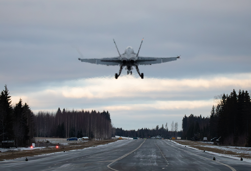 Hävittäjä on juuri noussut ilmaan. Kuvan alaosassa tie ja sivuilla puita.