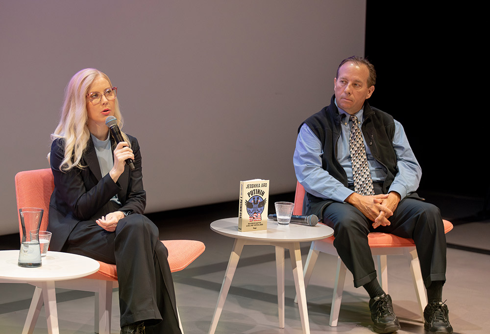 Aro ja Wiswesser istuvat paneelikeskustelussa. Aro puhuu mikrofoniinsa. Heidän välisellä pöydällä on Putinin USA -kirja.