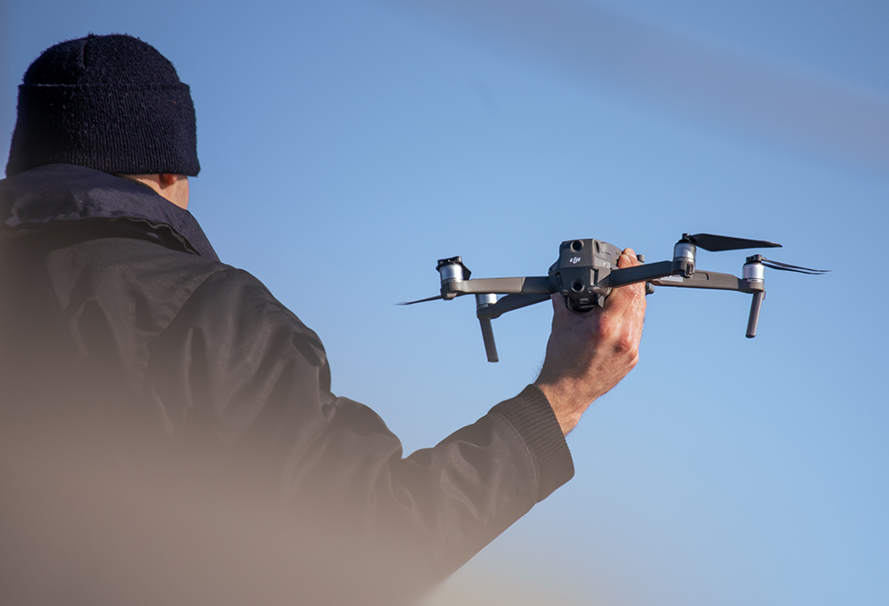 Takaata päin mustapukuinen henkilö pitelee dronea.