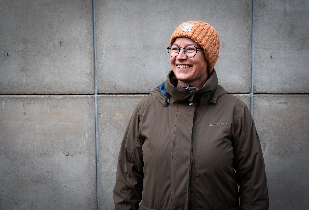 Sanna Matintalo hymyilee pipo päässään harmaan betoniseinän edessä.