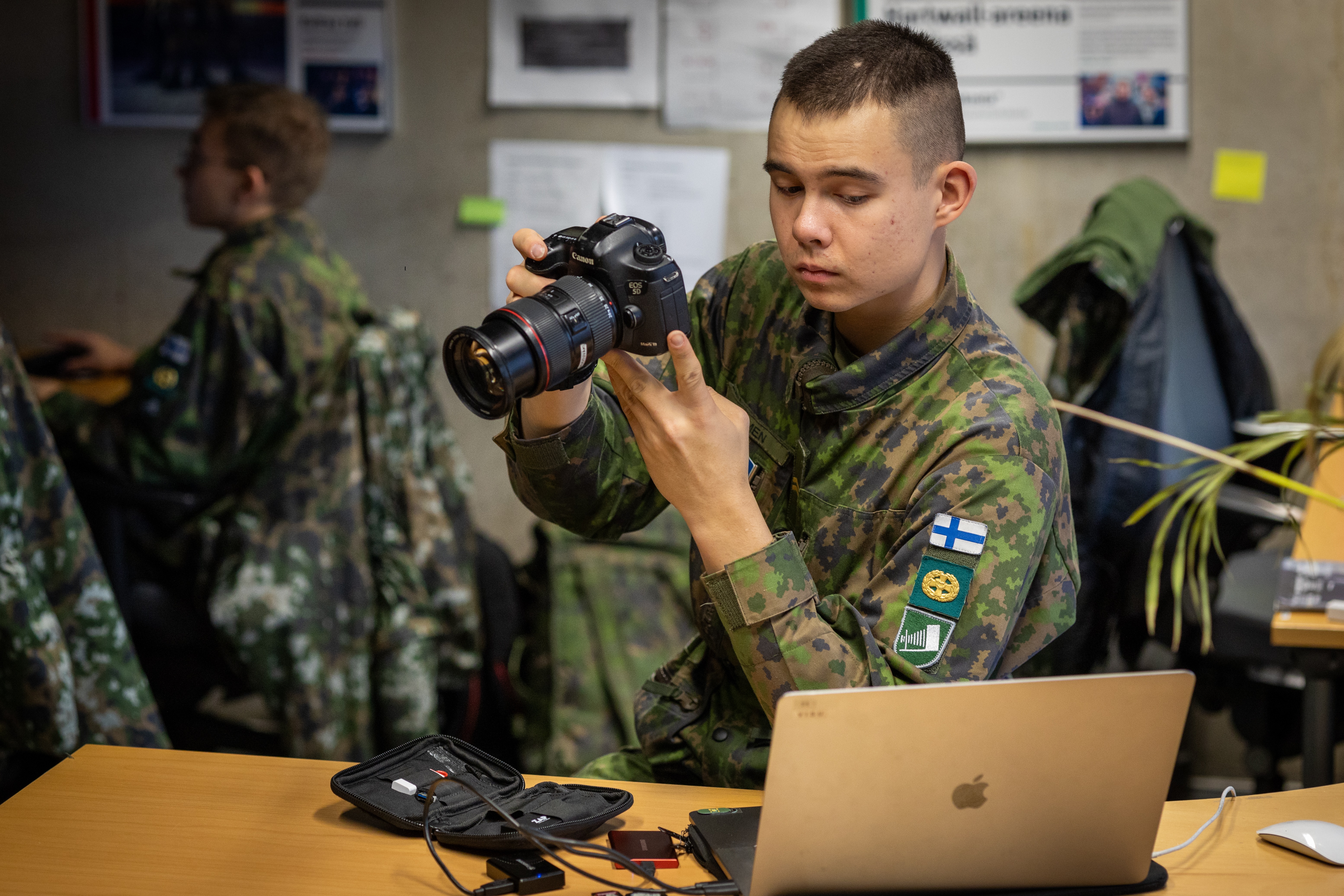 Kuvassa alikersantti Viljami Paimen kamera kädessään Ruotoväen toimistossa.