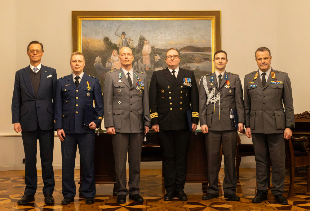 Palkitsija ja palkitut seisovat rivissä ja katsovat kameraan.