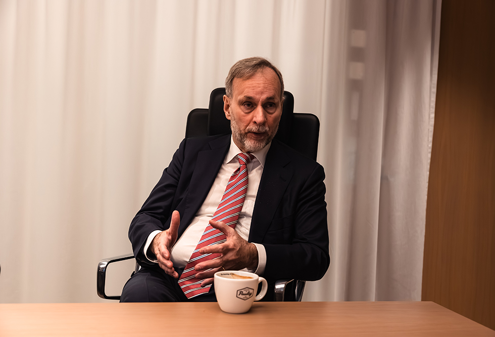 Esa Rautalinko istuu tuolilla pöydän ääressä. Hän puhuu elehtivästi. Pöydällä on kahvikuppi.