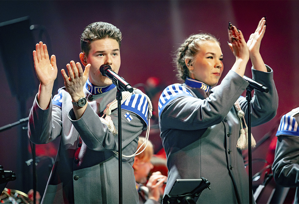 Kaksi reserviäistä sotilaan harmaissa vaatteissa esiintyvät lavalla ja taputtavat käsiään.