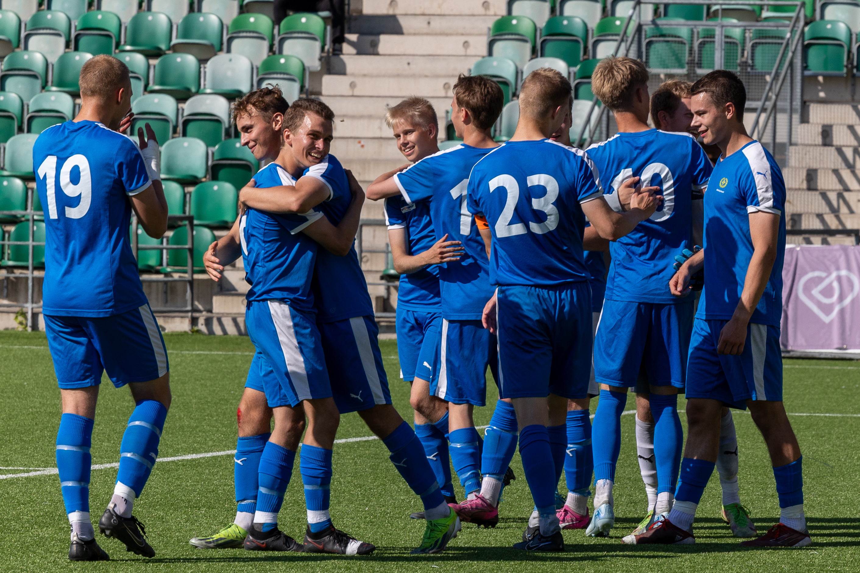 Pelipaitoihin pukeutuneet jalkapalloilijat juhlistavat voittoaan halaten pelikentällä.