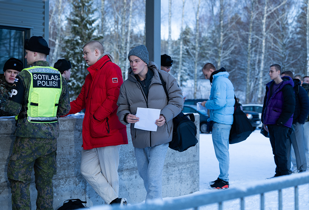 Uudet tulevat alokkaat jonottavat varuskunnan portilla talvisella säällä. Sotilaspoliisit tarkistavat jonottajien asiapapereita.