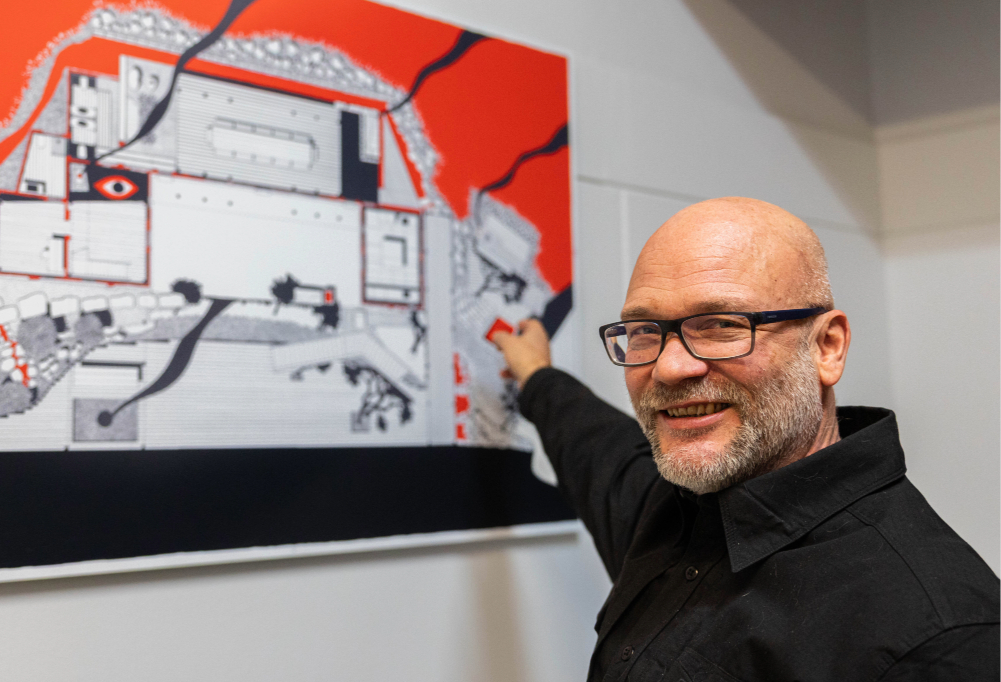 Marco Casagrande katsoo kameraan hymyillen ja osoittaa taulua.