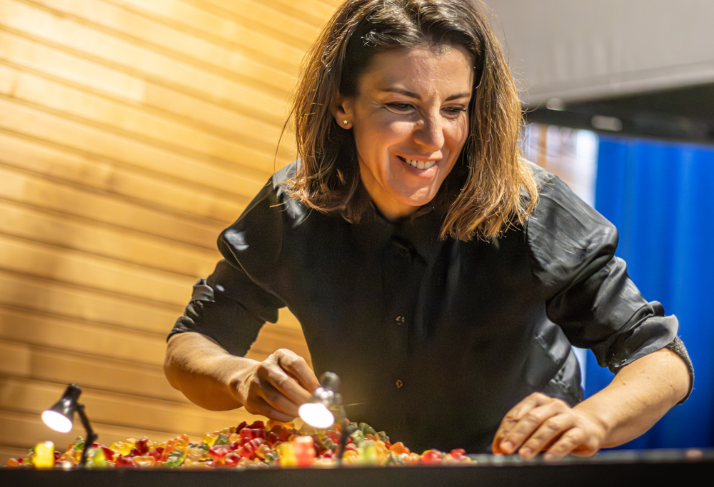 Naisnäyttelijä näyttämönä toimivan pöydän takana, jonka päällä on kasa nallekarkkeja.