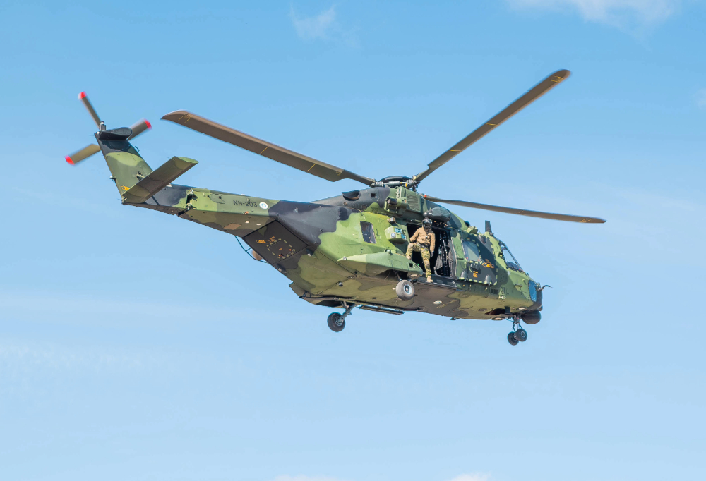 Kuvassa näkyy taivaalla lentävä maastokuvioinen NH90-helikopteri, jonka sisällä on sotilas.