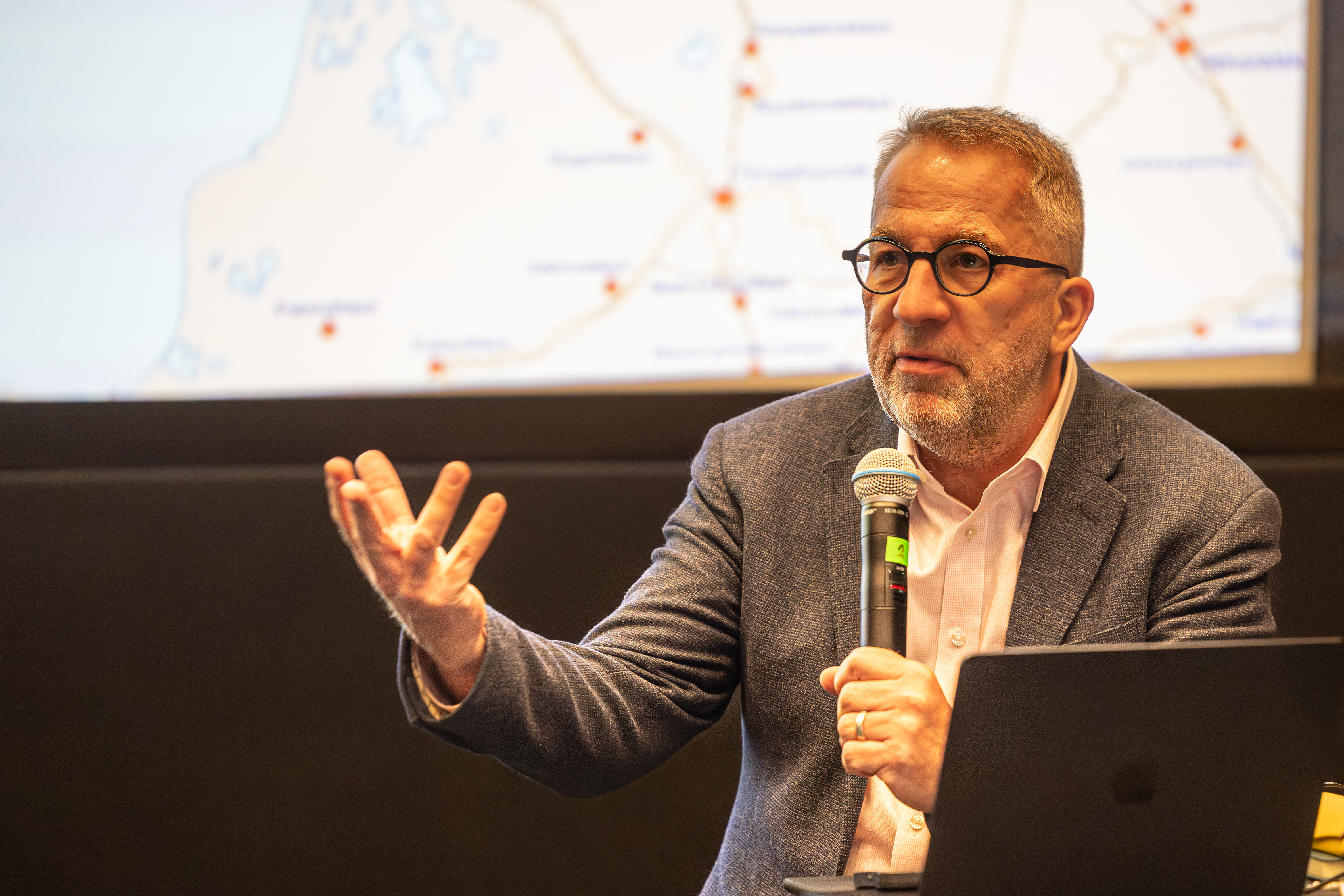 Exeterin yliopiston emeritusprofessori David Lewis istuu mikki kädessä ja toinen käsi hieman ojennettuna.