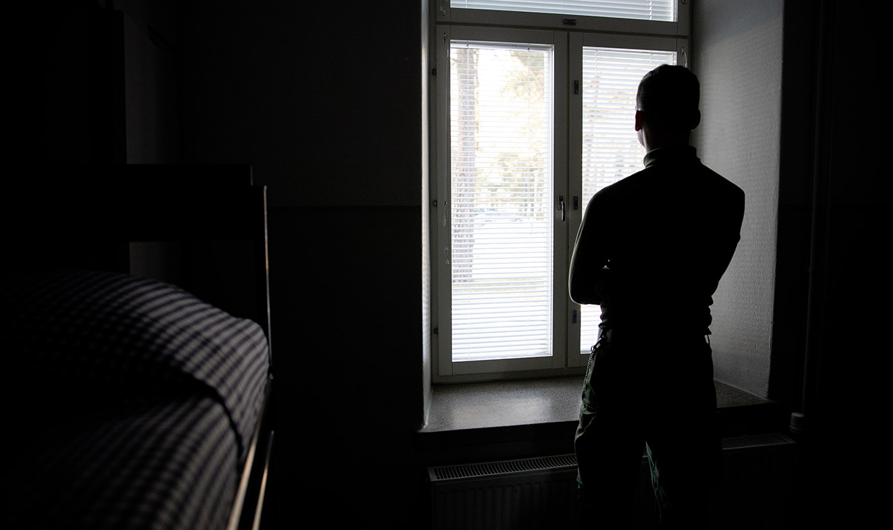 Kuvassa varusmies eristyksen kaltaisissa olosuhteissa katselemassa ulos ikkunasta.