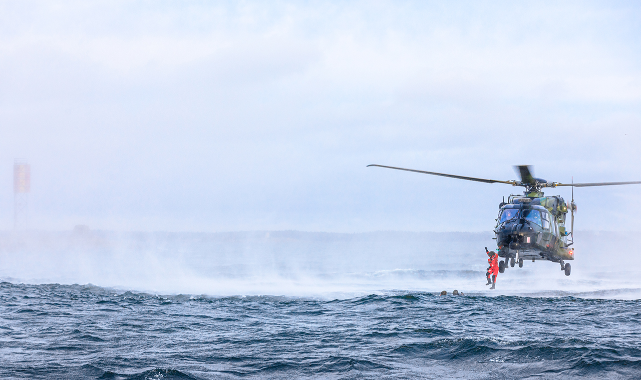 Kuvassa helikopteri ja pintapelastaja keskellä harjoitusta.