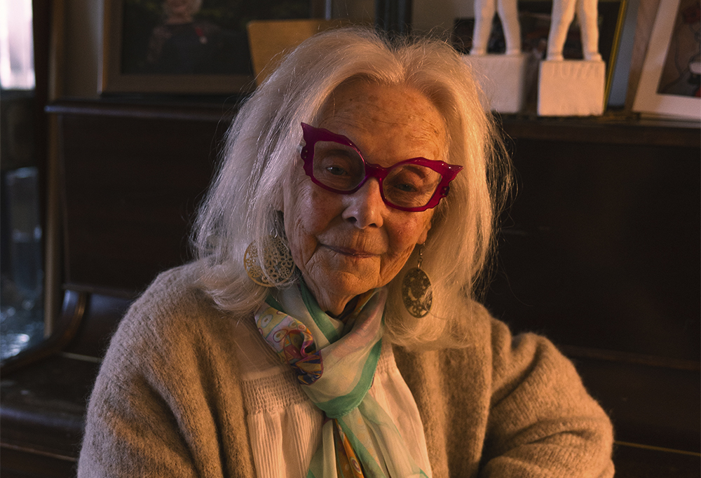 Seela Sella istuu pianoon nojaten ja katsoo kameraan.