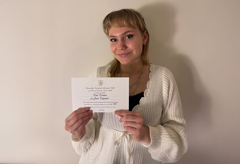 Tuuli Turunen hymyilee kameralle käsissään kutsu Linnan juhliin.