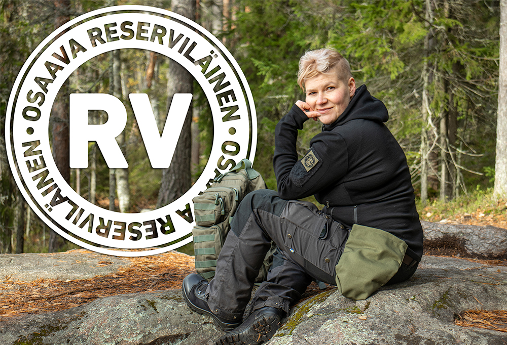 Mustanvihreissä patikointivaatteissa poseeraava Susanna Takamaa istuu kalliolla ja katsoo viekkaasti kameraan.