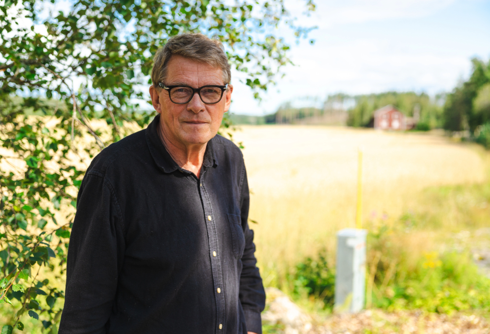 Matti Vanhanen seisoo ulkona peltomaiseman edessä ja katsoo kameraan.