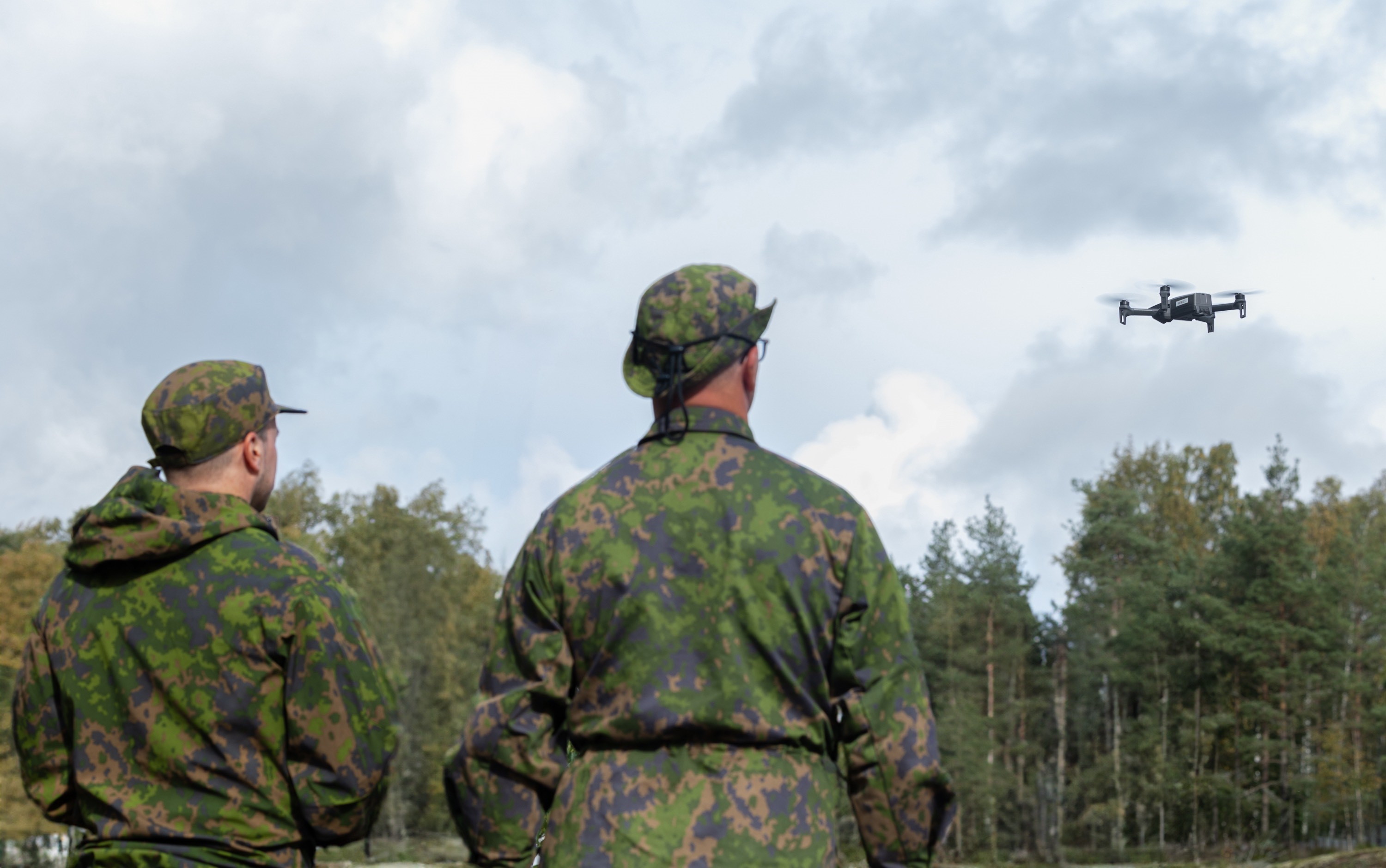 Kaksi sotilasta katsoo droonia, joka lentää