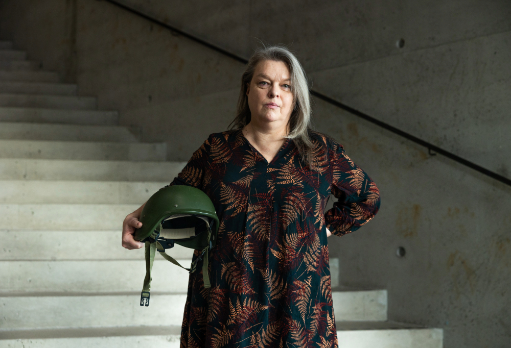 Kuvassa Elina Knihtilä katsoo kameraan sotilaskypärä kainalossaan.