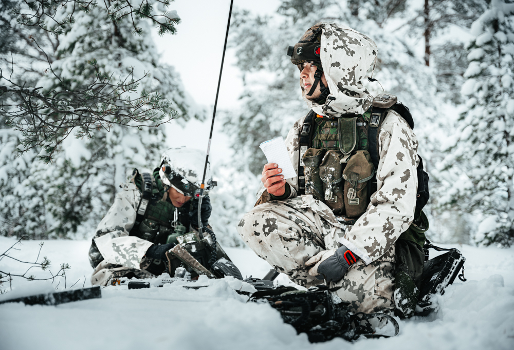 Kuvassa kaksi varusmiestä lumisessa metsässä.
