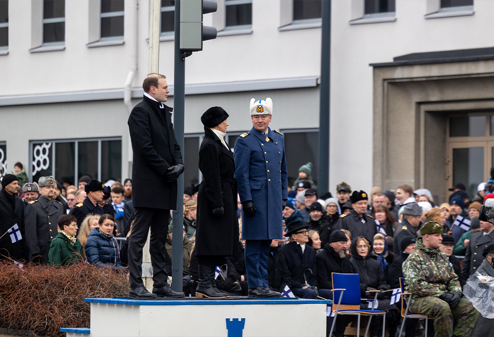 Henkilöt ovat odottamassa ohimarssia korokkeella.