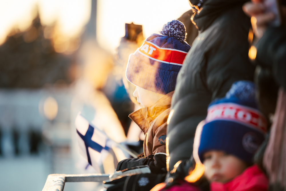 Kuvassa yleisöä ihailemassa paraatikatselmusta sekä Suomen lippu.