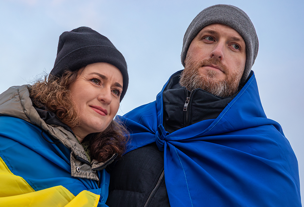 Oleksandr Butenko ja Hanna Franchuk ovat sonnustautuneet Ukrainan lippuihin. He katsovat oikeaan reunaan. Taustalla kirkas taivas.